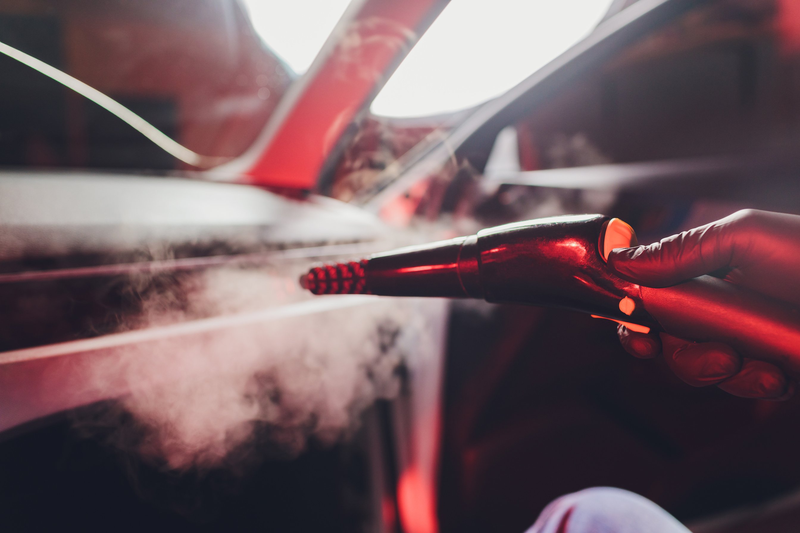 Handsome man cleaning car with hot steam.